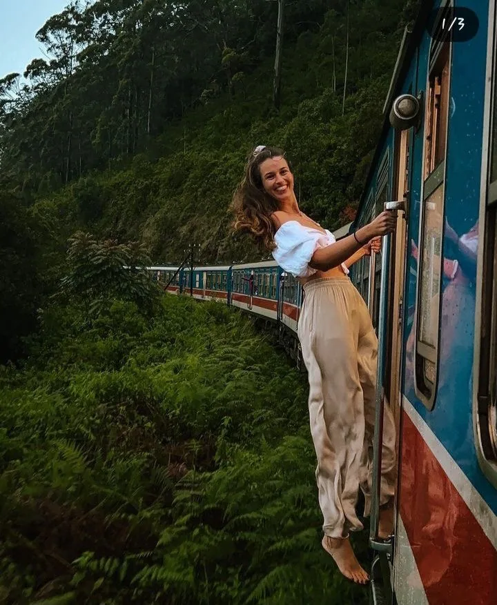 A traveler leans from a blue train as it winds through Sri Lanka's green hill country.