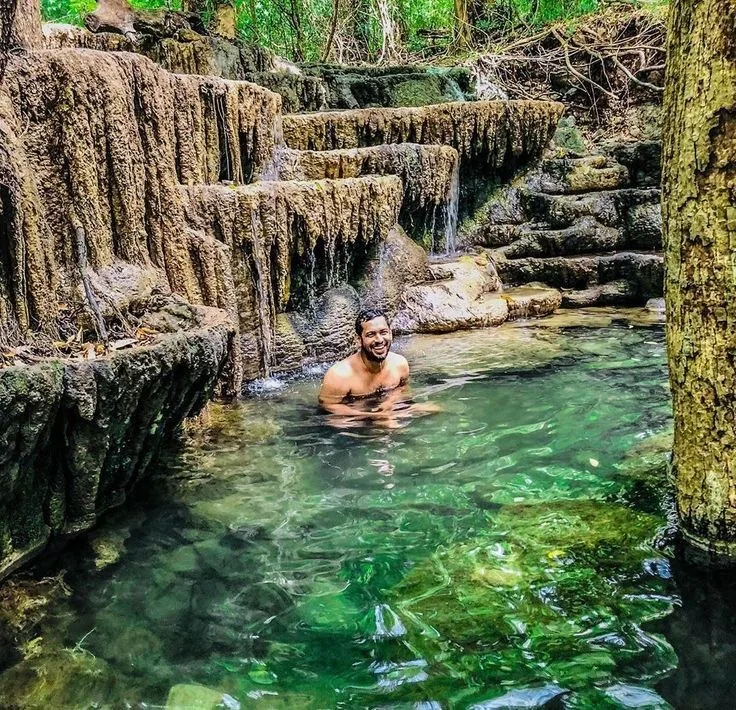 A traveler relaxes in a clear natural pool surrounded by sculpted rock and forest.