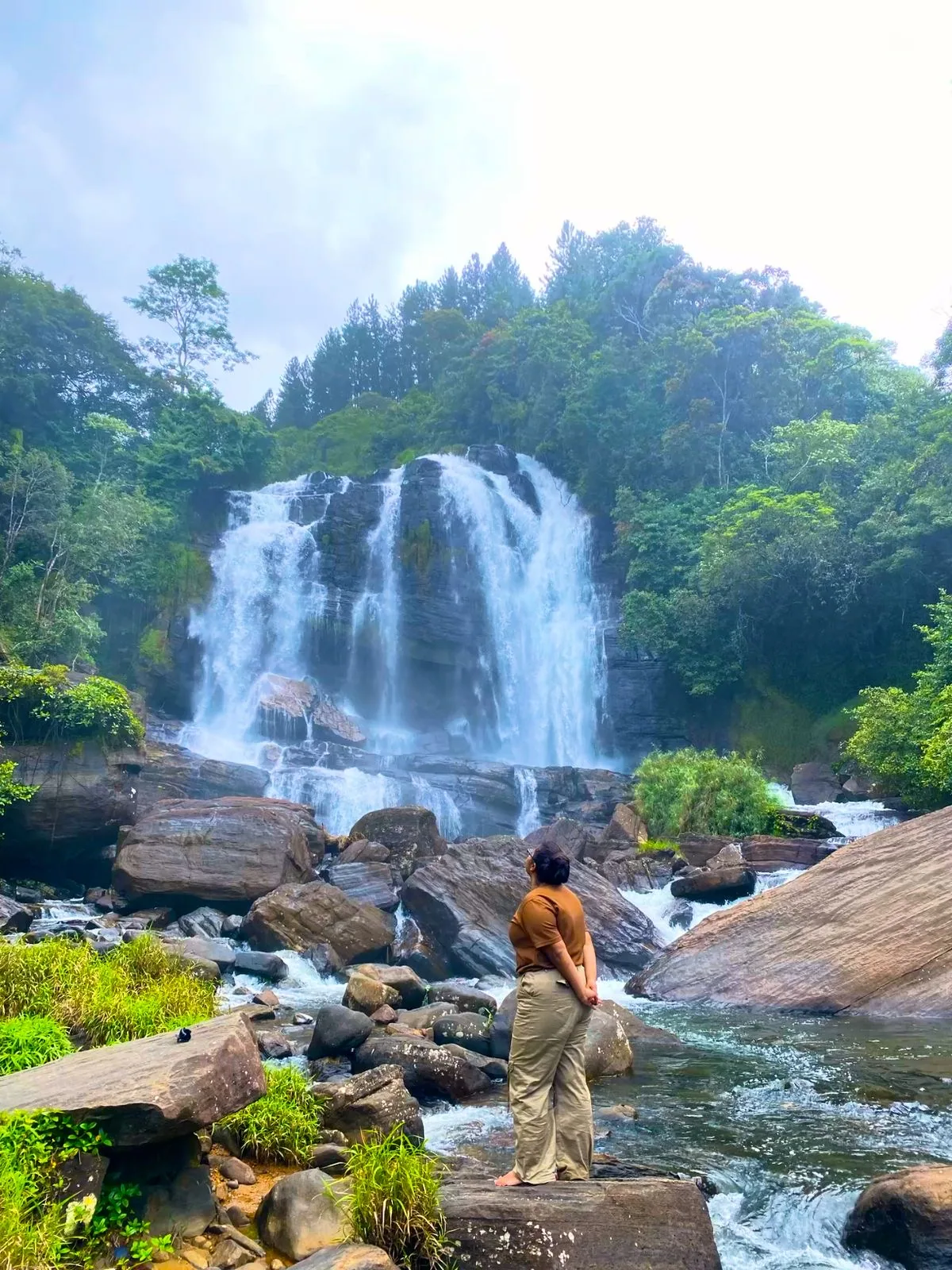A traveler takes in a broad waterfall from the rocks below.