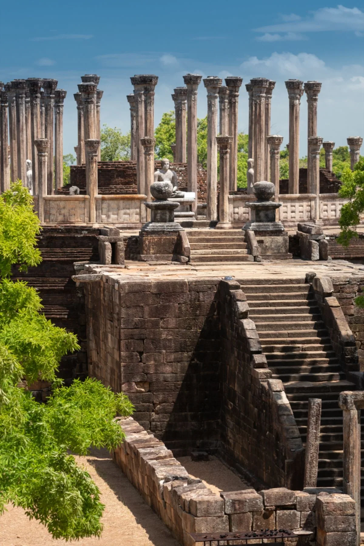 Weathered stone pillars stand beneath a bright blue sky at Polonnaruwa.