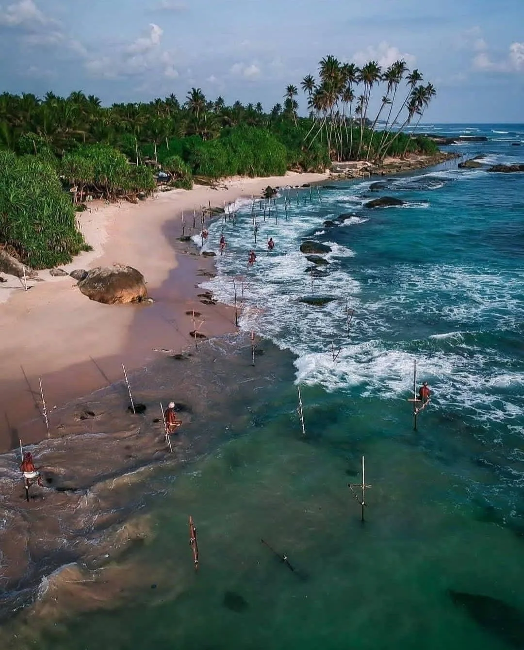 Stilt fishermen wait above the water along a palm-lined southern beach.